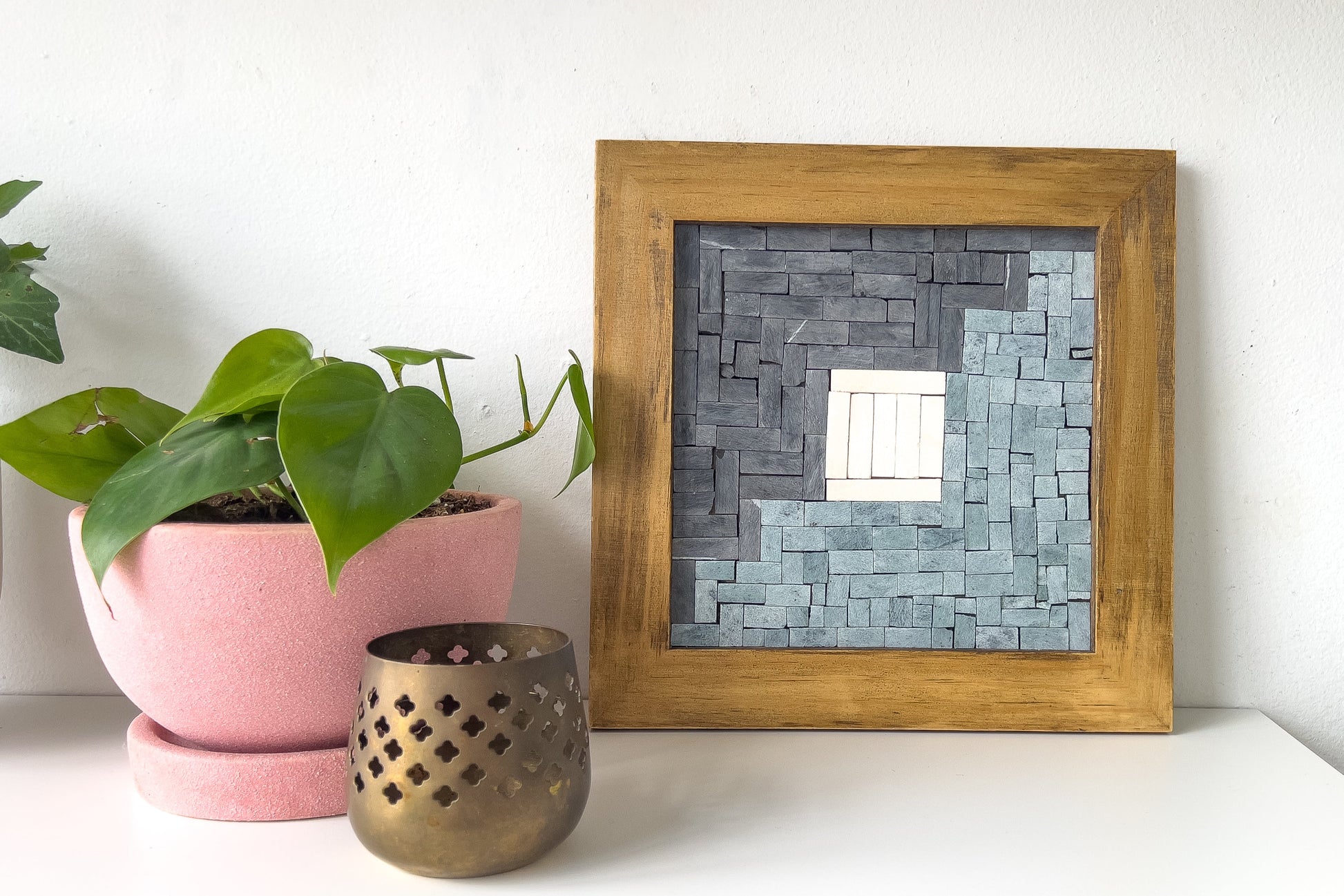Framed mosaic mirror on a white surface with a plant and candle holder.