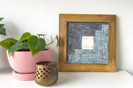 Framed mosaic mirror on a white surface with a plant and candle holder.